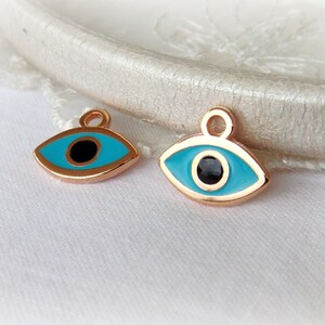 Puede incluir: Dos amuletos de ojo turco dorados con esmalte azul y centros negros. Los amuletos tienen un bucle en la parte superior para sujetarlos a joyas.