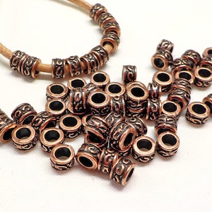 May include: A pile of copper-coloured metal beads with a decorative design. The beads are round and have a hole in the centre. They are perfect for jewellery making or other crafts.