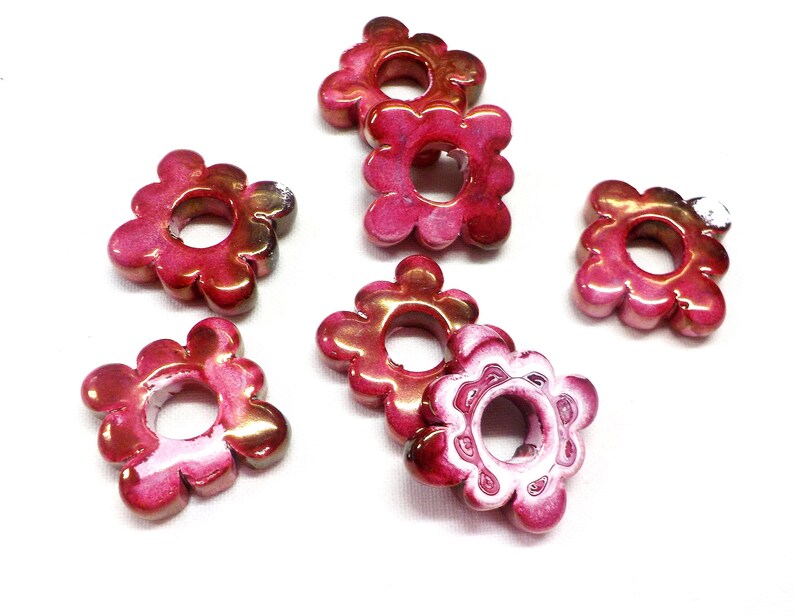 Puede incluir: Seis cuentas de color rosa y blanco con forma de flor y un agujero en el centro. Las cuentas tienen un acabado brillante.