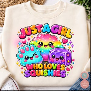 Op de afbeelding: Een cr&egrave;mekleurig sweatshirt met een kleurrijke afbeelding en de tekst "JUST A GIRL WHO LOVES SQUISHIES". Het ontwerp bevat drie lachende cartoonfiguren: een regenboogwolk, een blauwe pootvormige figuur en een paarse kubus.