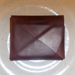 May include: A folded burgundy leather wallet on a white surface.