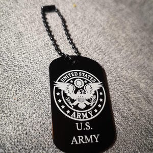 Könnte beinhalten: Schwarzer Metall-Dogtag mit einem weißen, gravierten Bild des Siegels der US-Armee und dem Text "UNITED STATES ARMY" und "U.S. ARMY".