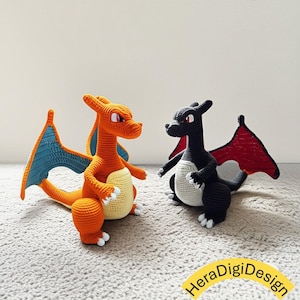 May include: Two crochet dragon figures. One is orange with blue wings and a cream belly, the other is black with red wings and a cream belly. Both have white claws and are posed facing each other. The figures are on a light gray surface.