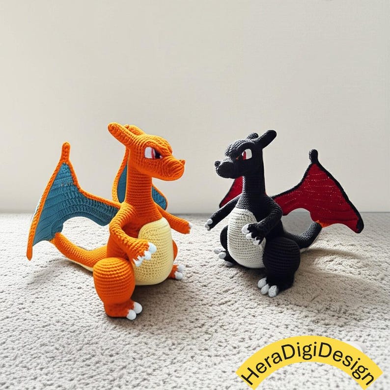 May include: Two crochet dragon figures. One is orange with blue wings and a cream belly, the other is black with red wings and a cream belly. Both have white claws and are posed facing each other. The figures are on a light gray surface.
