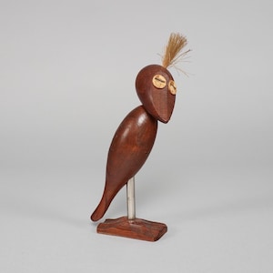Puede incluir: Un abridor de botellas de madera con forma de pájaro con un acabado marrón. El pájaro tiene un pico largo y delgado y una cabeza pequeña y redonda. Tiene dos ojos pequeños y redondos y un mechón de plumas marrones en la parte superior de la cabeza. El pájaro está de pie sobre una pequeña base rectangular.