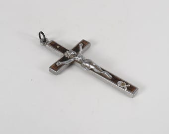 Puede incluir: Un crucifijo de plata y madera con una detallada representación de Jesucristo. La cruz presenta una incrustación de madera oscura y un marco de metal. En la parte superior hay un pequeño lazo para colgar. Un símbolo religioso tradicional.