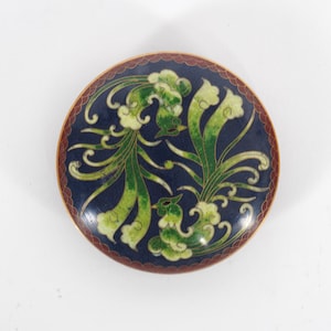 Op de afbeelding: Ronde cloisonné schaal met een donkerblauwe achtergrond en een decoratief ontwerp met groene en witte gestileerde vogels en bladeren. De rand is donkerrood met een gouden rand.