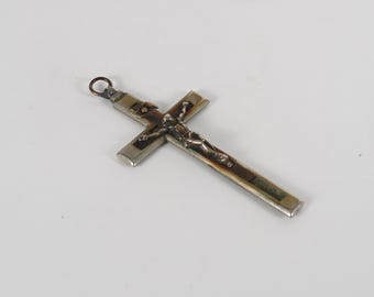 Puede incluir: Un crucifijo plateado con una detallada figura de Jesucristo. La cruz tiene una incrustación marrón oscuro y un pequeño lazo en la parte superior para colgar. La figura está intrincadamente detallada.