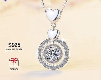 May include: A silver necklace with a round pendant featuring a large clear stone surrounded by smaller stones. The pendant is attached to a chain with two smaller heart-shaped charms. The necklace is labeled "S925 Sterling Silver" and comes in a gift box.