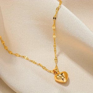Pu&ograve; includere: Una collana a catena dorata con un ciondolo a forma di cuore. La catena &egrave; composta da piccoli ovali collegati.