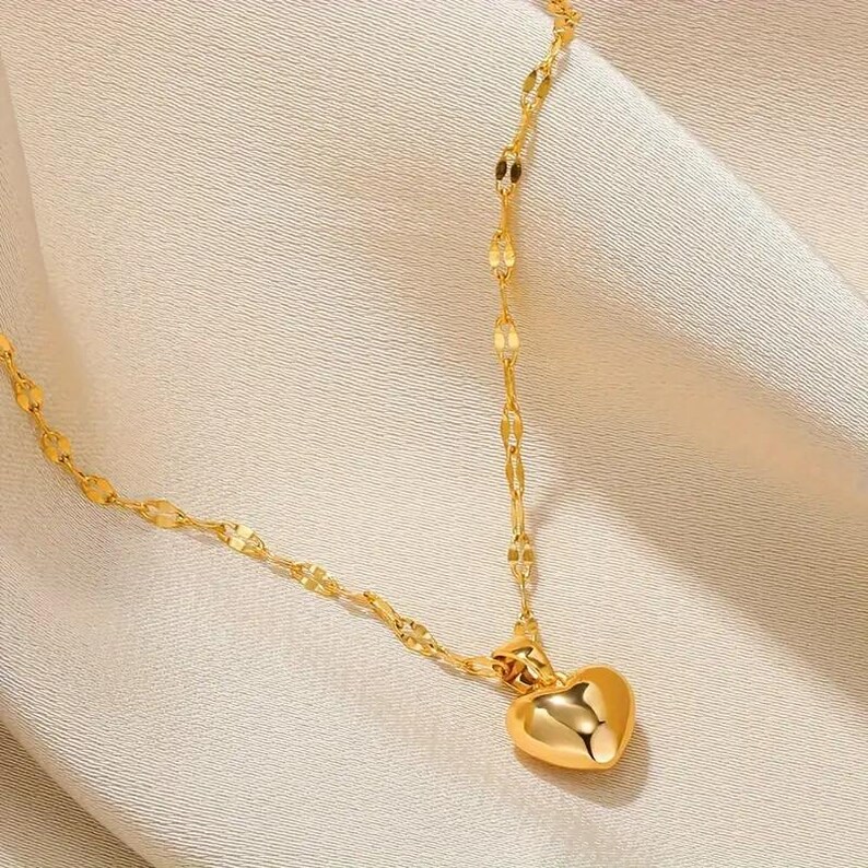 Pu&ograve; includere: Una collana a catena dorata con un ciondolo a forma di cuore. La catena &egrave; composta da piccoli ovali collegati.