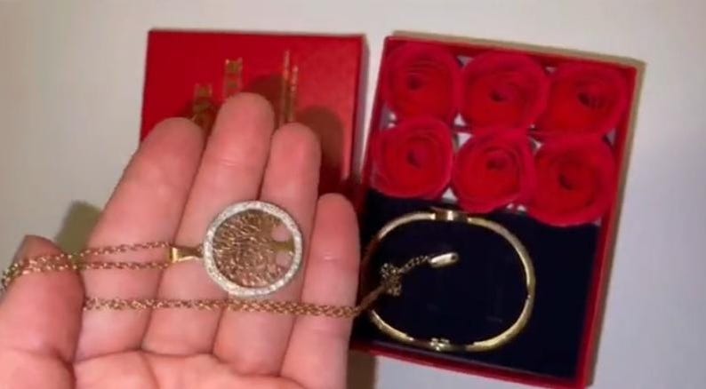 May include: A gold necklace with a tree of life pendant and a gold bracelet in a red box with six red roses.
