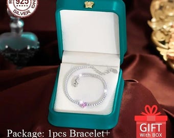 May include: A silver bracelet with a pink heart charm and clear cubic zirconia stones, displayed in a teal jewelry box. The box has a gold crown on the lid. The text "REAL STERLING 925 SILVER" is on a silver tag. The text "GIFT With BOX" is on a red and white gift box.