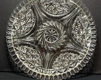 May include: Clear glass serving dish with a starburst and geometric pattern. The dish has a scalloped edge and is divided into sections. The centre has a spiral design. A decorative piece for serving appetizers or desserts.