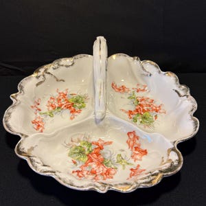 May include: A white porcelain serving dish with a handle. The dish is divided into three sections and features a floral design with orange and green flowers. The rim of the dish is decorated with gold trim.