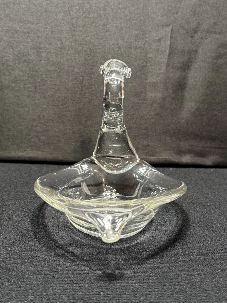 May include: Clear glass swan-shaped dish with a flared base and a long, curved neck. The dish has a shallow, square-shaped bowl. The glass is transparent, allowing light to pass through, and the design is simple and elegant.