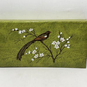 May include: A rectangular box with a textured olive green surface featuring a brown bird perched on a dark branch with white blossoms. The bird has a long tail and a white wing patch. The design is centered on the front of the box.