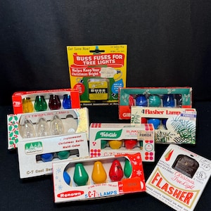 May include: Assortment of vintage Christmas light accessories, including replacement bulbs, fuses, and a flasher unit. The packaging features colorful designs and text, with the words "Yuletide" and "Renown" visible. The items are displayed on a black surface.