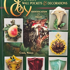 May include: A book cover titled McCoy Pottery Wall Pockets & Decorations Identification & Values by Craig Nissen. The cover features a dark green background with multiple photographs of ceramic wall pockets, including floral, bird, and owl designs.