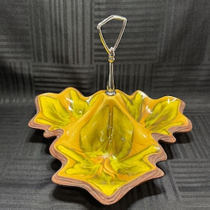 May include: A decorative serving dish in the shape of a leaf, featuring a vibrant yellow and brown color scheme. The dish has a silver handle and a detailed leaf design, perfect for serving snacks or small items.