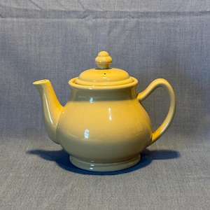 May include: A pale yellow ceramic teapot with a rounded body and a lid with a small knob on top.