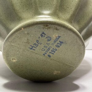 May include: Close-up of a sage green ceramic bowl with a fluted design. The bottom of the bowl has the text "Haeger U.S.A. PATENT DESIGN #195 034" in blue ink. The bowl has a speckled texture.
