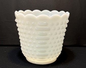 May include: A white hobnail glass planter with a scalloped rim. The planter has a textured surface with raised dots and horizontal bands. The base is a lighter shade of white. The planter is likely for indoor use.