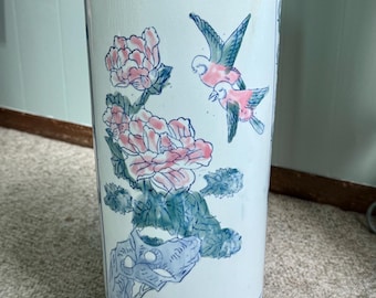 May include: A cylindrical ceramic umbrella stand featuring a white base with hand-painted blue and pink floral motifs and two birds in flight. The top and bottom rims are decorated with intricate blue geometric and repeating patterns.