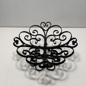 May include: A black, decorative metal object with an ornate, symmetrical design. The object features swirling, scroll-like patterns and heart-shaped accents. It is likely a decorative piece for a home or event.