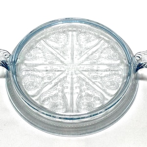 Peut inclure: Couvercle rond en verre transparent, teinté de bleu clair. Le couvercle présente des motifs floraux gravés et deux poignées. Le centre du couvercle porte l'inscription "Pyrex".