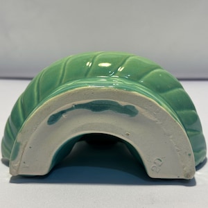 May include: A semi-circular ceramic mold in a glossy mint green glaze with a ribbed, swirling pattern. The base is unglazed white ceramic, featuring a visible number 22 stamped into the material, showing the underside of the kitchenware item.