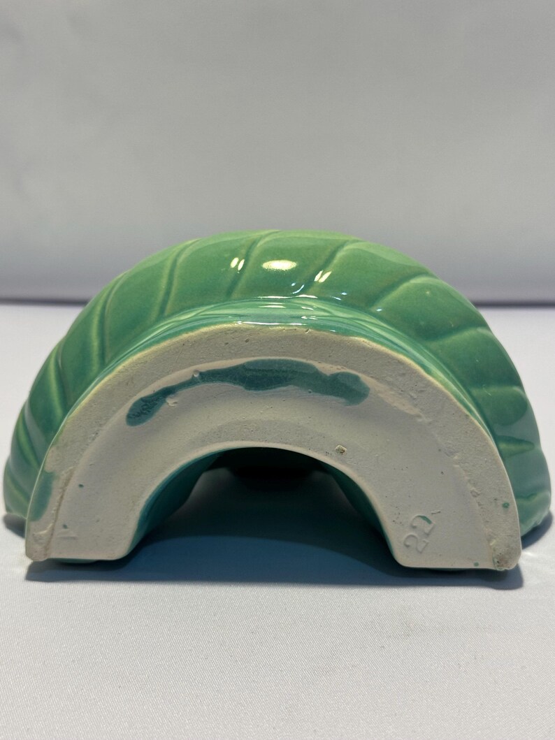 May include: A semi-circular ceramic mold in a glossy mint green glaze with a ribbed, swirling pattern. The base is unglazed white ceramic, featuring a visible number 22 stamped into the material, showing the underside of the kitchenware item.