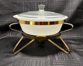 Cazuela vintage de vidrio opalino Glasbake con calentador de metal tono dorado.