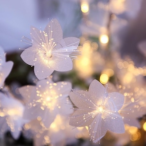 Puede incluir: Un grupo de flores artificiales blancas de cinco pétalos con filamentos de fibra óptica en el centro que emiten una luz cálida y brillante. Los pétalos tienen una apariencia texturizada y ligeramente translúcida, creando un suave efecto bokeh.
