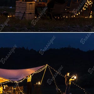 May include: Nighttime camping scene with a tent illuminated by string lights. A person is holding a lantern. The scene includes camping chairs, storage containers, and a dark background of trees and a night sky.