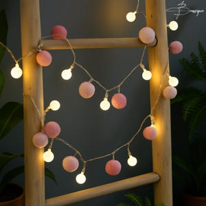 May include: A string of decorative lights featuring alternating round pink fabric spheres and small glowing white bulbs. The lights are arranged on a thin, clear wire, creating a soft illumination effect with a mix of solid and light-emitting elements.
