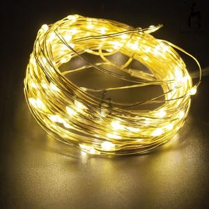 May include: A coiled strand of thin, flexible copper wire featuring numerous small, glowing warm white LED lights. The wire is wound into a circular shape, creating a dense cluster of illumination that emits a soft, bright light throughout.
