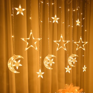 May include: A string of warm white LED curtain lights featuring hanging star and crescent moon shapes. The decorative lighting arrangement consists of multiple vertical strands with illuminated five-pointed stars and crescent moons.