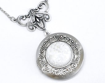 May include: A silver locket necklace with a filigree design. The locket has a round, white, iridescent center.