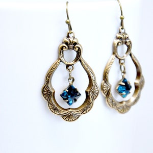 May include: A pair of gold-tone dangle earrings with a blue crystal drop. The earrings feature a delicate, ornate design with a filigree pattern.
