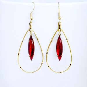 May include: Gold hoop earrings with a dangling red teardrop-shaped crystal.