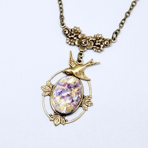 May include: A gold necklace with a floral design and a pendant featuring a bird and an iridescent glass oval.