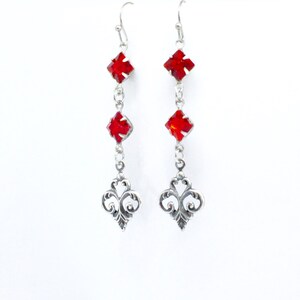 Peut inclure: Boucles d'oreilles pendantes en argent avec trois pierres de cristal rouges et un motif en filigrane en bas.