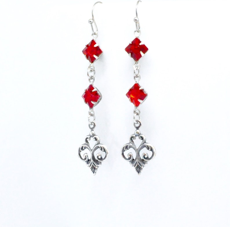 Peut inclure: Boucles d'oreilles pendantes en argent avec trois pierres de cristal rouges et un motif en filigrane en bas.