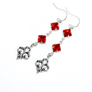 Peut inclure: Boucles d'oreilles pendantes en argent avec trois cristaux carr&eacute;s rouges et un motif de filigrane d&eacute;coratif en bas.