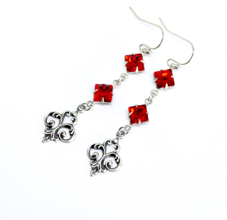 Peut inclure: Boucles d'oreilles pendantes en argent avec trois cristaux carr&eacute;s rouges et un motif de filigrane d&eacute;coratif en bas.