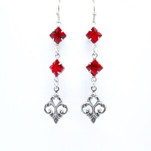 Peut inclure: Boucles d'oreilles pendantes en argent avec trois cristaux carr&eacute;s rouges et un motif en filigrane en bas.