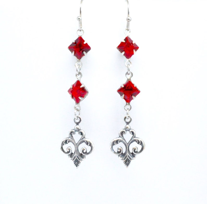 Peut inclure: Boucles d'oreilles pendantes en argent avec trois cristaux carr&eacute;s rouges et un motif en filigrane en bas.