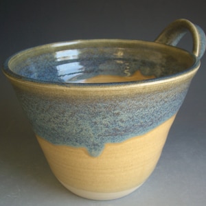 May include: A ceramic mug with a blue and yellow glaze. The mug has a wide, rounded shape and a single handle.