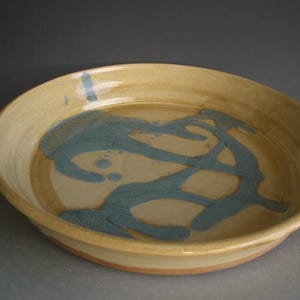 May include: A ceramic serving dish with a light brown glaze and a blue glaze design. The blue glaze is in a swirling pattern.